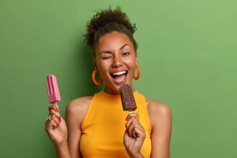Mulher jovem sorridente segurando dois picolés, ilustrando a dieta gelada após extrair o dente do siso na Odonto Esthetic Master em Cruz Alta.