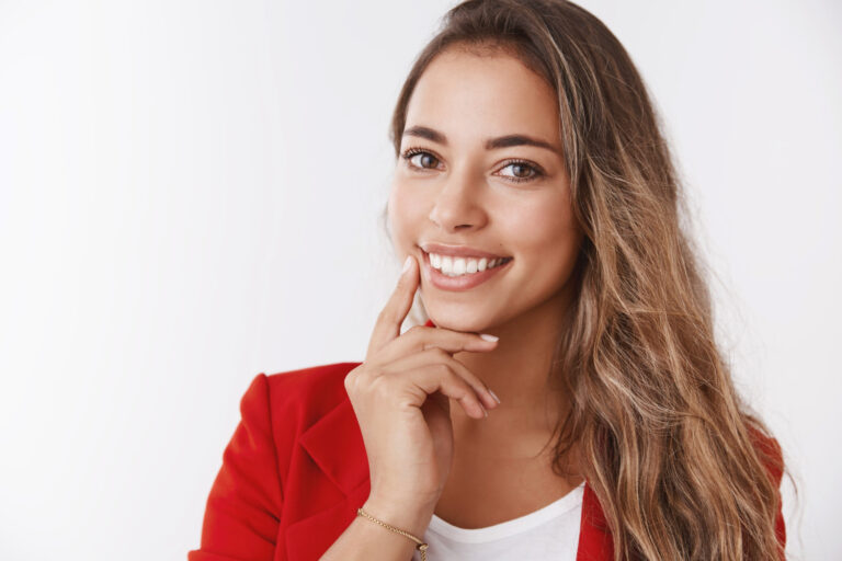 Mulher de blazer vermelho sorrindo e tocando os lábios após preenchimento labial com dentista em Cruz Alta na Odonto Esthetic Master.