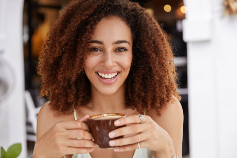 Mulher sorrindo ao tomar café, destacando a resistência ao manchamento das lentes de contato dental na clínica em Cruz Alta - RS.